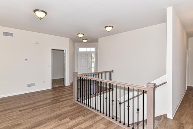 corridor with baseboards, visible vents, wood finished floors, and an upstairs landing