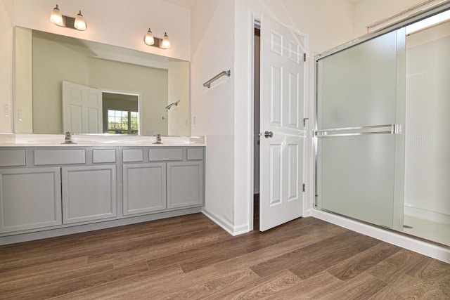 bathroom with double vanity, a stall shower, a sink, and wood finished floors