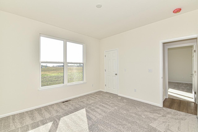 empty room with carpet floors, visible vents, and baseboards