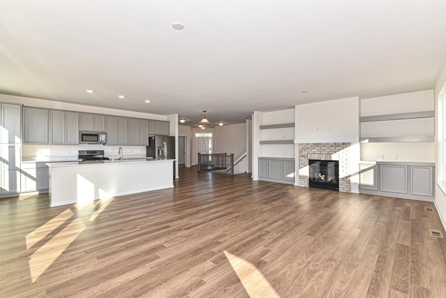 kitchen featuring light wood finished floors, stainless steel appliances, gray cabinets, a kitchen island with sink, and a sink