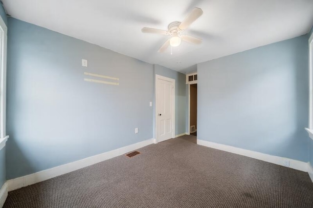 unfurnished room featuring a ceiling fan, visible vents, dark carpet, and baseboards