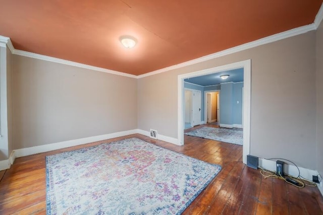 empty room with wood-type flooring, visible vents, baseboards, and crown molding