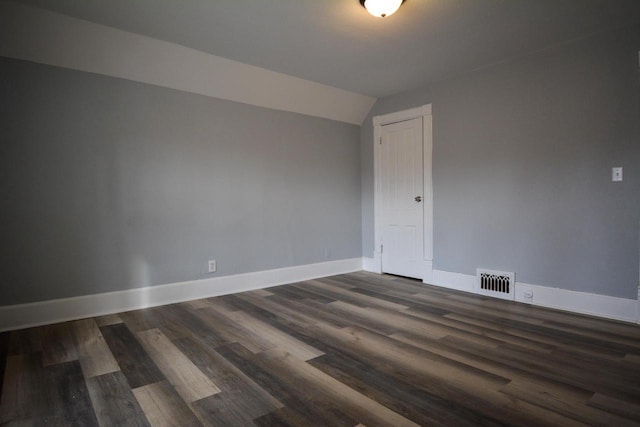 spare room with vaulted ceiling, dark wood-type flooring, visible vents, and baseboards