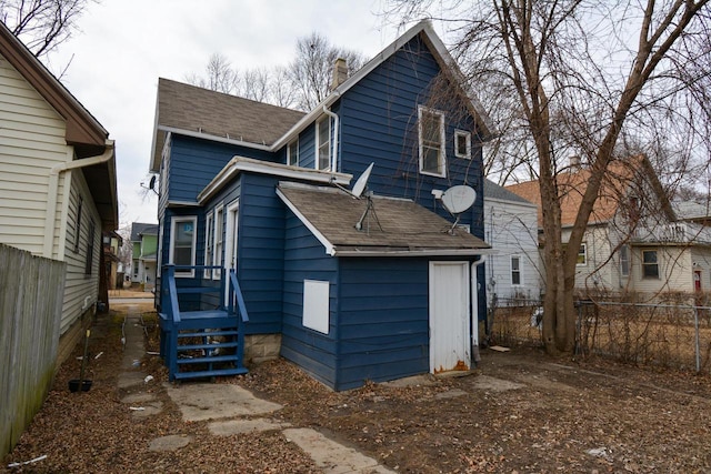 rear view of house featuring roof with shingles, a chimney, and fence