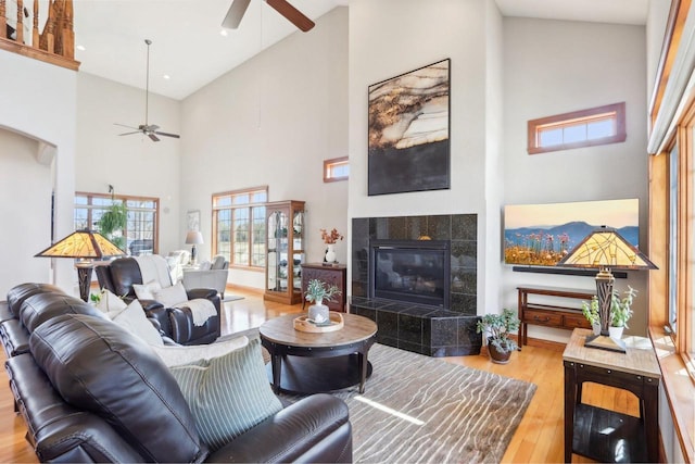 living room with a ceiling fan, high vaulted ceiling, wood finished floors, and a tiled fireplace