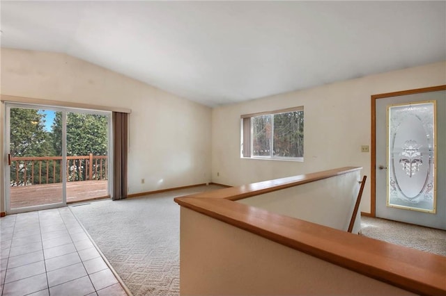 spare room with lofted ceiling, light tile patterned floors, baseboards, and light colored carpet