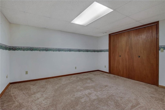 unfurnished bedroom with carpet floors, a closet, a drop ceiling, and baseboards