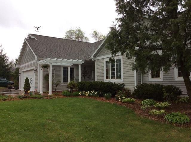 view of front facade with a garage, a shingled roof, a front lawn, and a pergola