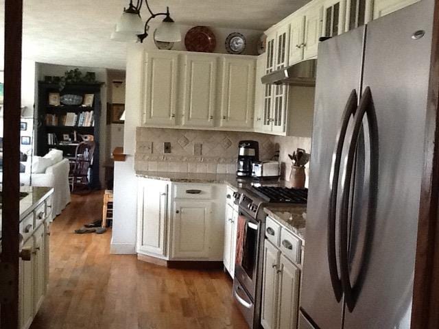 kitchen featuring under cabinet range hood, stainless steel appliances, light stone counters, and wood finished floors