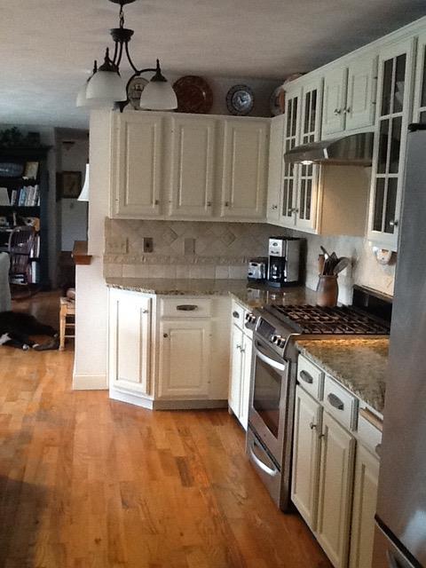 kitchen with light stone counters, light wood finished floors, glass insert cabinets, under cabinet range hood, and appliances with stainless steel finishes