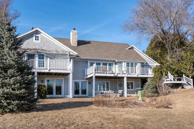 rear view of house featuring a lawn, french doors, a shingled roof, a wooden deck, and a chimney