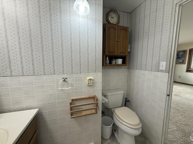 bathroom featuring toilet, tile walls, wainscoting, wallpapered walls, and vanity