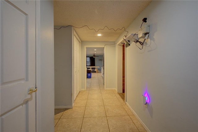 hallway with a textured ceiling, light tile patterned flooring, and baseboards