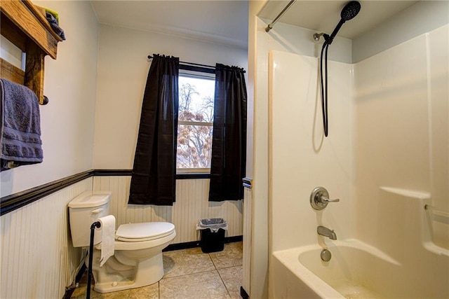 full bath featuring shower / washtub combination, a wainscoted wall, toilet, and tile patterned floors