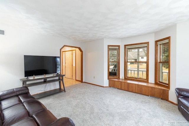 carpeted living room featuring baseboards, visible vents, and arched walkways