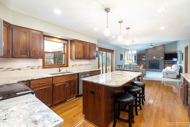 kitchen featuring a sink, light wood-style floors, a brick fireplace, a center island, and dishwasher