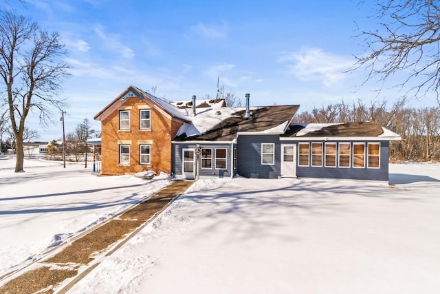 snow covered house featuring a sunroom