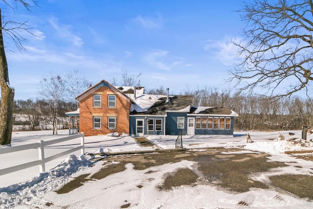 view of front facade with a sunroom, brick siding, fence, and driveway