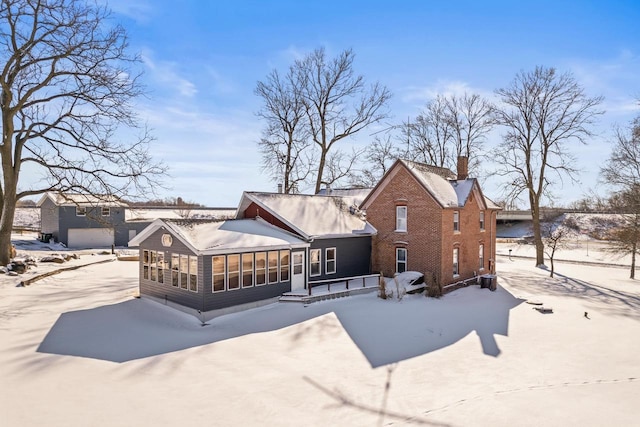 snow covered rear of property with a sunroom, brick siding, and a chimney