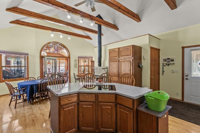 kitchen featuring light wood-style flooring, a center island, vaulted ceiling with beams, a wood stove, and black electric cooktop