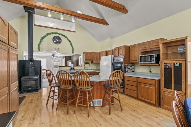 kitchen with visible vents, stainless steel microwave, a kitchen breakfast bar, freestanding refrigerator, and a wood stove