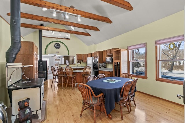 dining room featuring light wood finished floors, beamed ceiling, and a wood stove