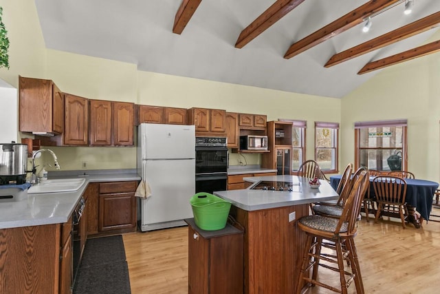 kitchen featuring light wood-style flooring, a sink, brown cabinets, a center island, and black appliances