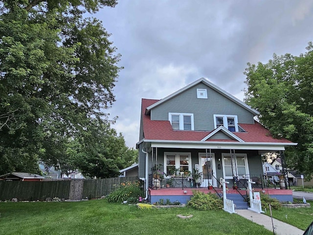 view of front of property featuring covered porch, roof with shingles, a front yard, and fence