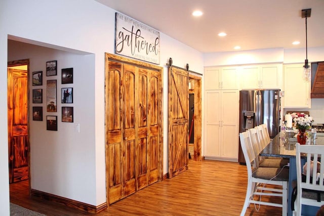 kitchen with a barn door, stainless steel fridge with ice dispenser, wood finished floors, and recessed lighting