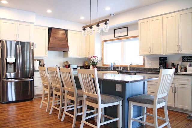 kitchen with custom range hood, appliances with stainless steel finishes, dark wood-style flooring, a center island, and a kitchen bar