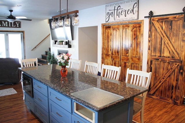 kitchen with ceiling fan, a barn door, a breakfast bar, dark wood-style flooring, and a center island