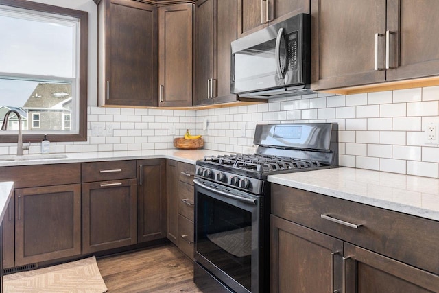 kitchen with stainless steel appliances, a sink, dark brown cabinets, and dark wood-style floors