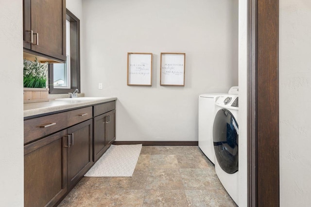 washroom with cabinet space, washing machine and dryer, stone finish floor, a sink, and baseboards