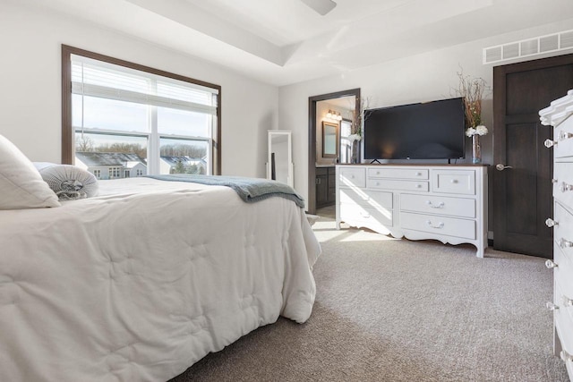 bedroom featuring ensuite bath, visible vents, a raised ceiling, and light colored carpet