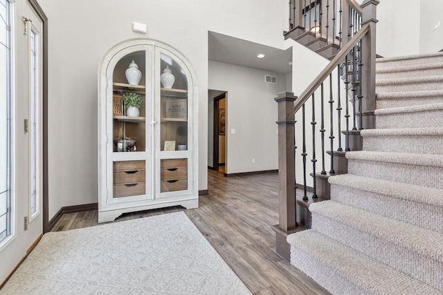 entrance foyer with visible vents, stairway, a high ceiling, wood finished floors, and baseboards