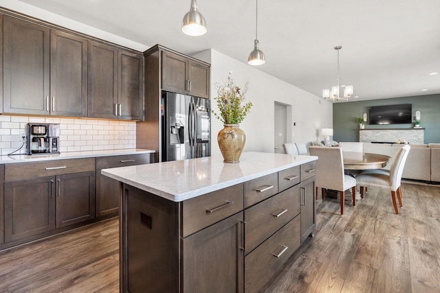 kitchen featuring dark wood-style flooring, open floor plan, stainless steel refrigerator with ice dispenser, backsplash, and decorative light fixtures