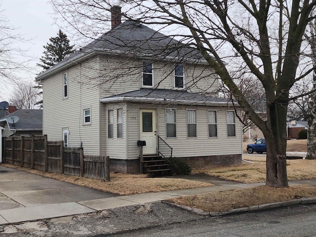 view of front facade with entry steps, a chimney, and fence