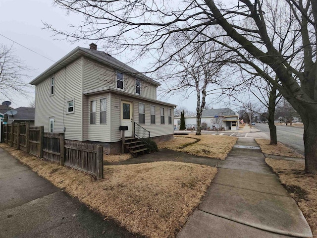 view of side of property featuring entry steps, fence, and a chimney