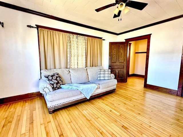 living room featuring baseboards, light wood-type flooring, a ceiling fan, and crown molding