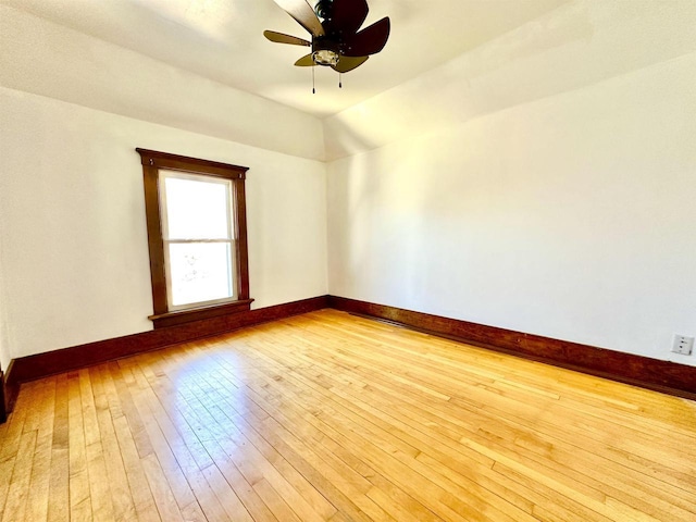 spare room with a ceiling fan, vaulted ceiling, light wood-style flooring, and baseboards