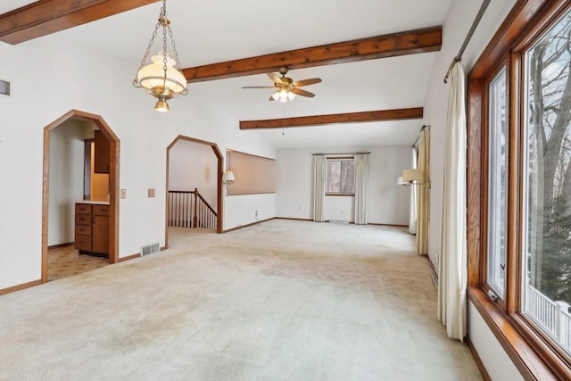 unfurnished living room with arched walkways, beamed ceiling, light carpet, and baseboards