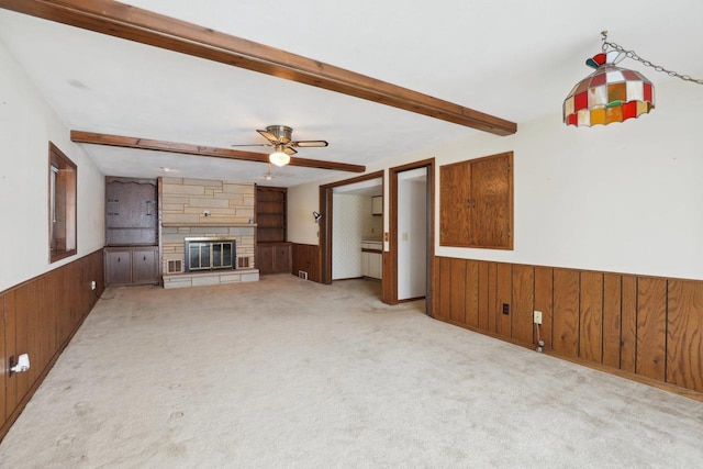 unfurnished living room featuring wooden walls, a wainscoted wall, carpet floors, a fireplace, and beamed ceiling