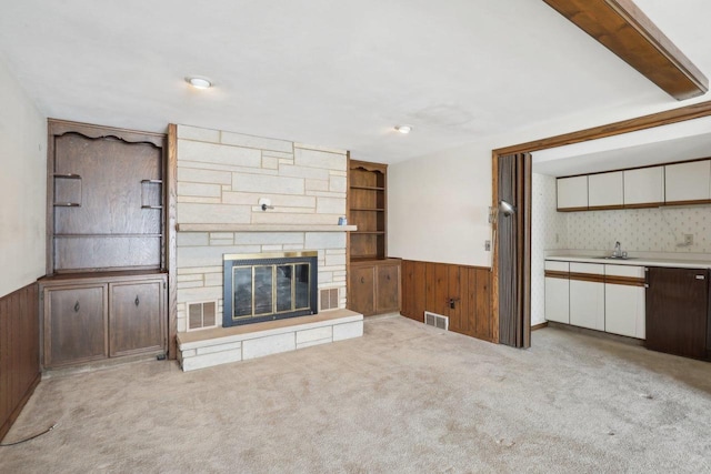 unfurnished living room with a wainscoted wall, visible vents, a fireplace, and carpet flooring