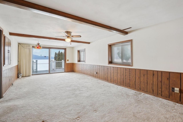 carpeted empty room featuring ceiling fan, beamed ceiling, wainscoting, and wooden walls