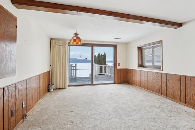 carpeted empty room with a wainscoted wall, wooden walls, and beamed ceiling