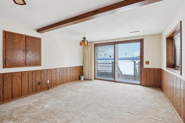 carpeted spare room with wooden walls, beam ceiling, and wainscoting