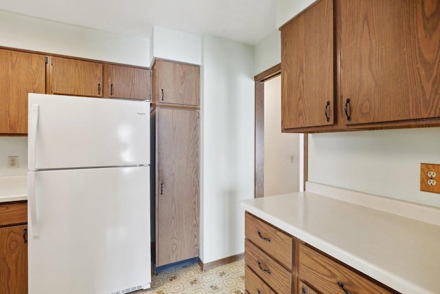 kitchen featuring light countertops, brown cabinetry, freestanding refrigerator, and light floors