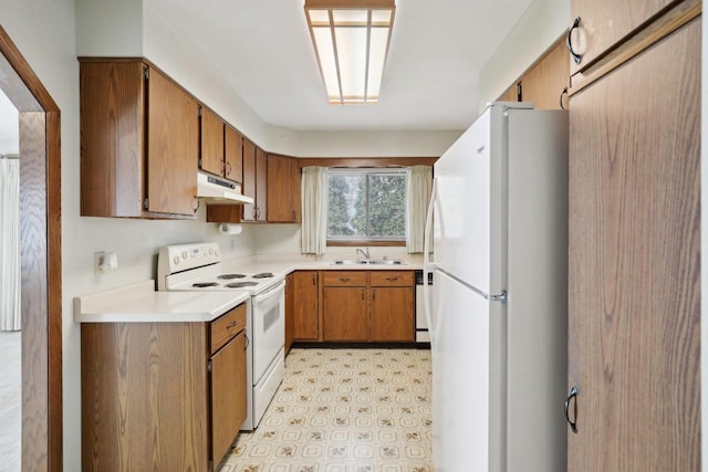 kitchen featuring under cabinet range hood, white appliances, a sink, light floors, and brown cabinetry