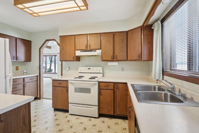 kitchen featuring arched walkways, light countertops, a sink, white appliances, and under cabinet range hood