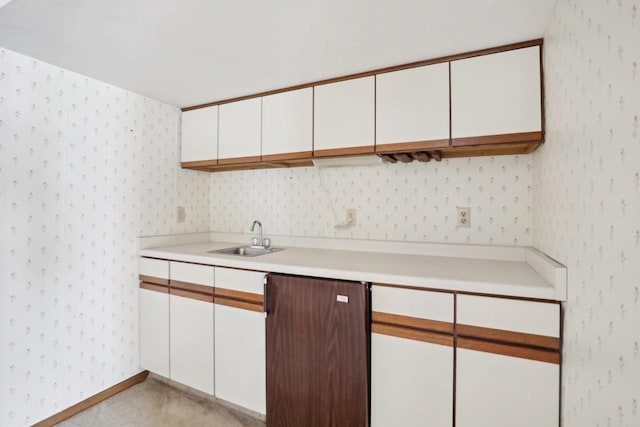 kitchen featuring light countertops, white cabinets, a sink, baseboards, and wallpapered walls